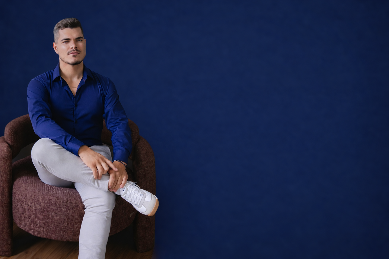 Victor Ribeiro sentado em uma poltrona, diante de um fundo azul-marinho